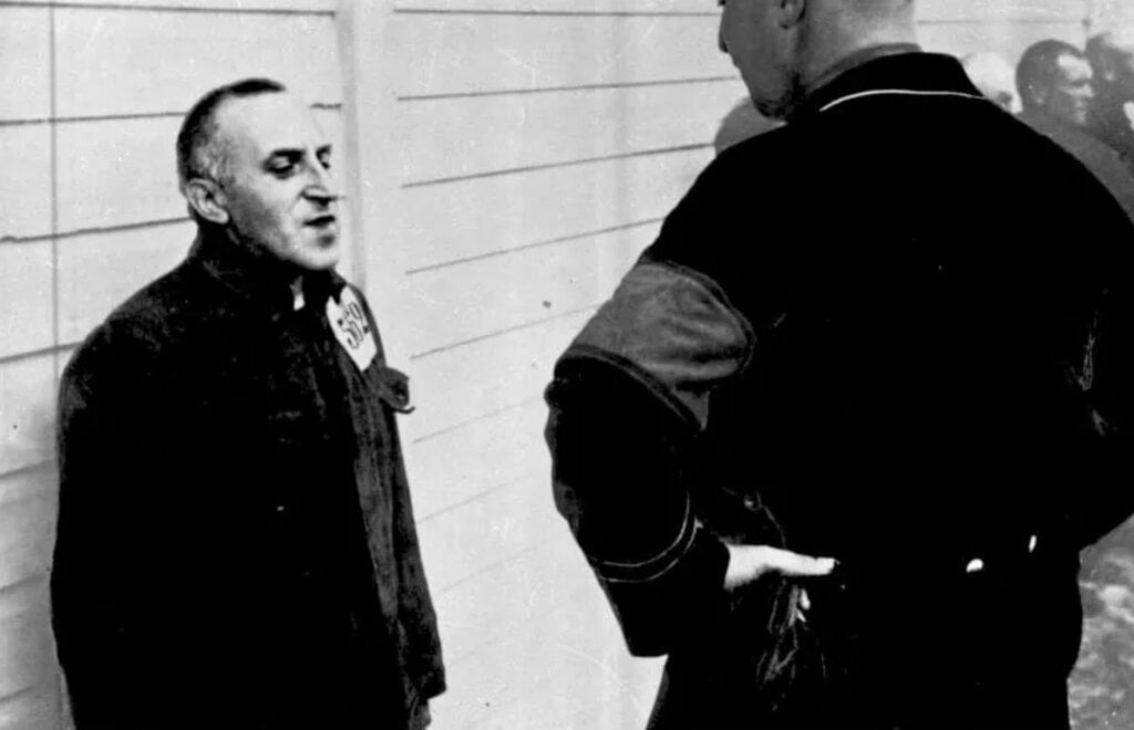 Carl von Ossietzky as a prisoner at the Esterwegen concentration camp, standing against a wall in front of a guard.