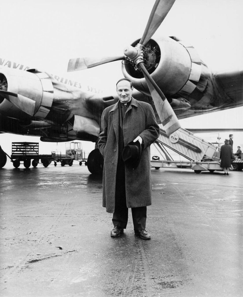 Father Georges Pire standing in front of an airplane