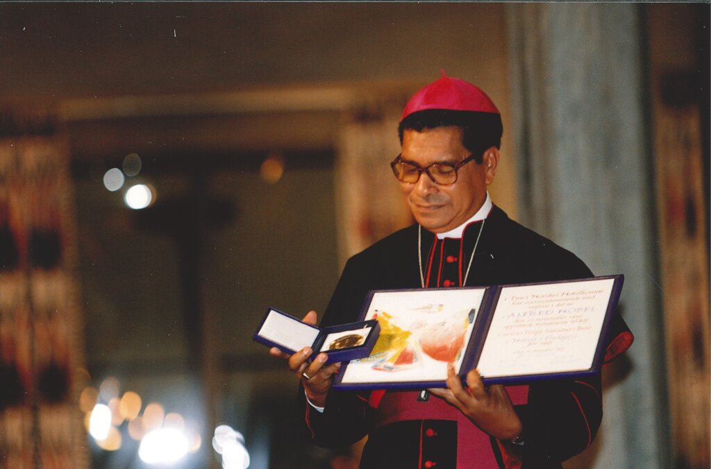 A bishop showing a medal and a diploma