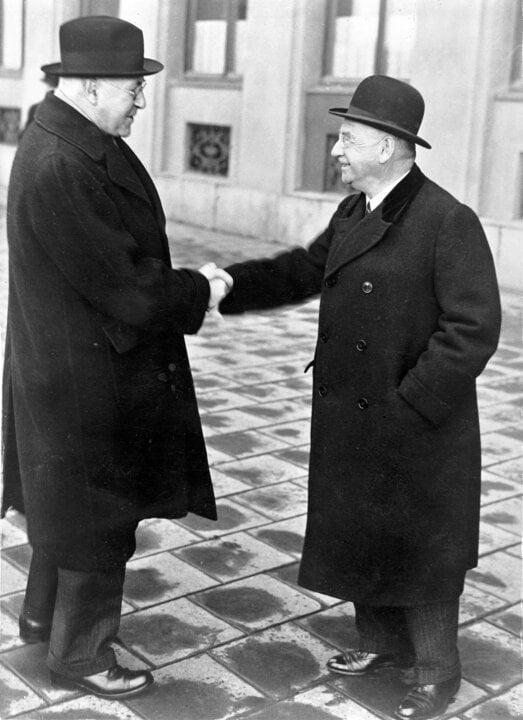 Two men in long coats shaking hands