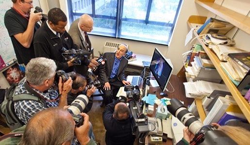 Saul Perlmutter in his office, surrounded by journalists