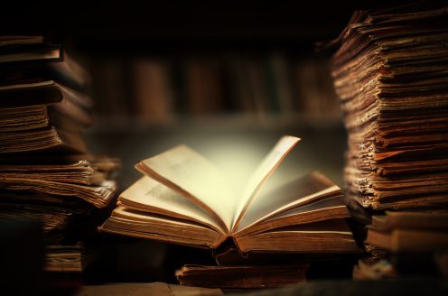 Magical book lying open on desk in library. Glowing pages illuminates surrounding.